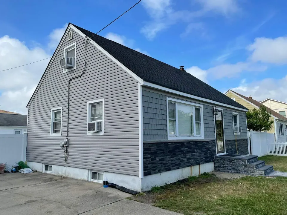 A small house with a gray siding and a black roof.