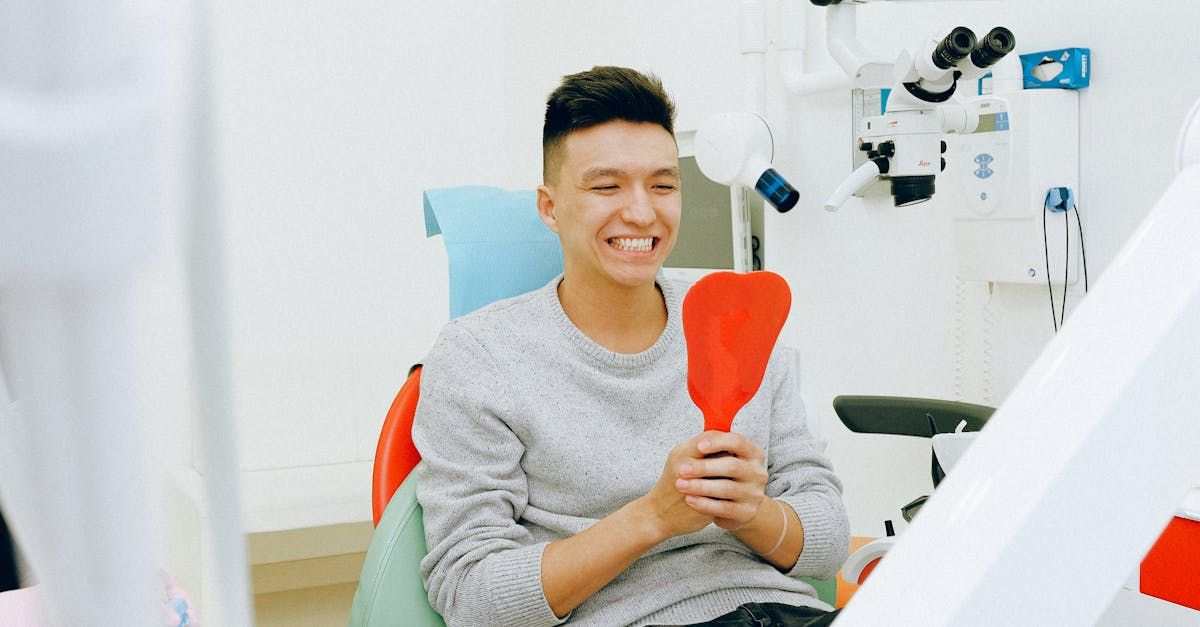 A man is sitting in a dental chair looking at his teeth in a mirror.