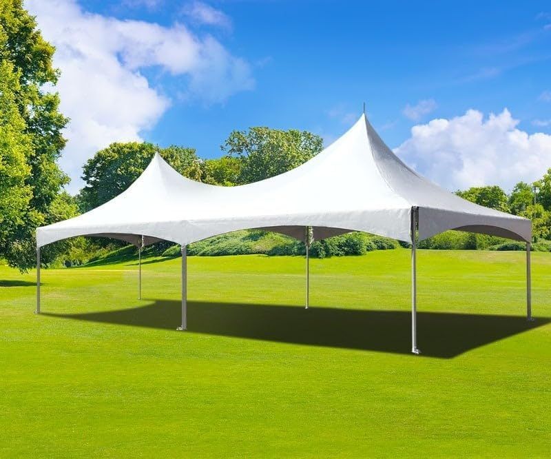 A white high-peak tent stands on a lush green lawn under a bright blue sky with scattered clouds.