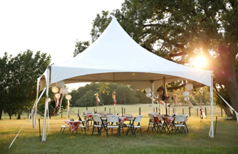 A white tent set up on a grassy lawn at sunset, featuring tables and chairs arranged for an outdoor event.