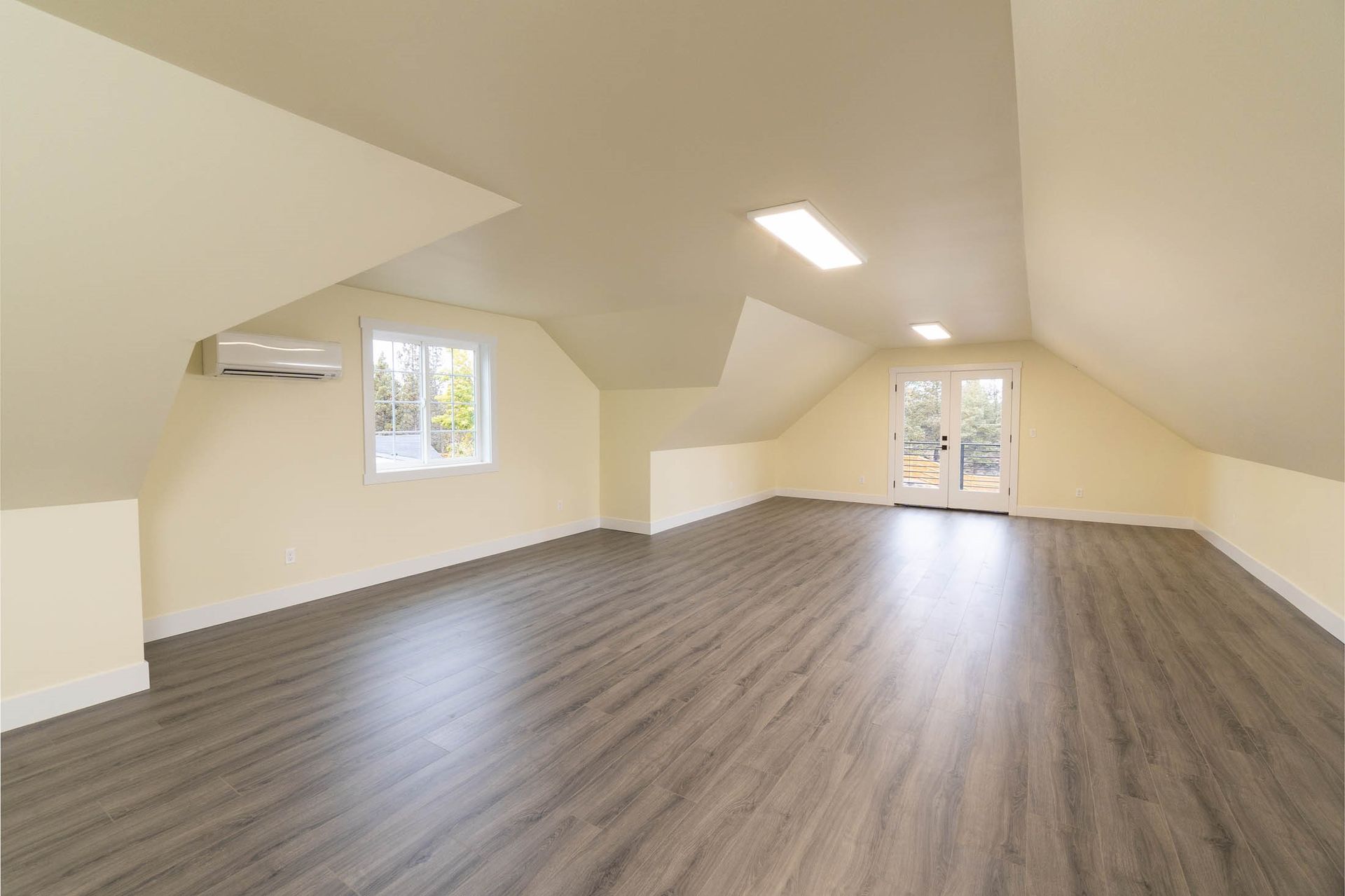 An empty attic with hardwood floors and a ceiling fan.