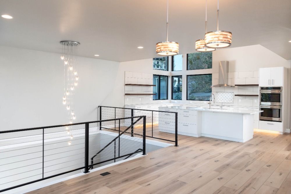A kitchen with white cabinets and wooden floors and a black railing.