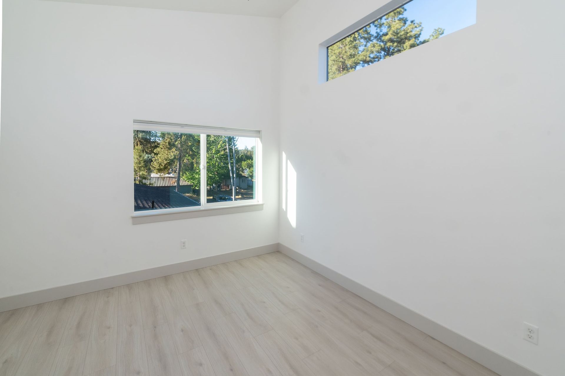 An empty room with two windows and a wooden floor.
