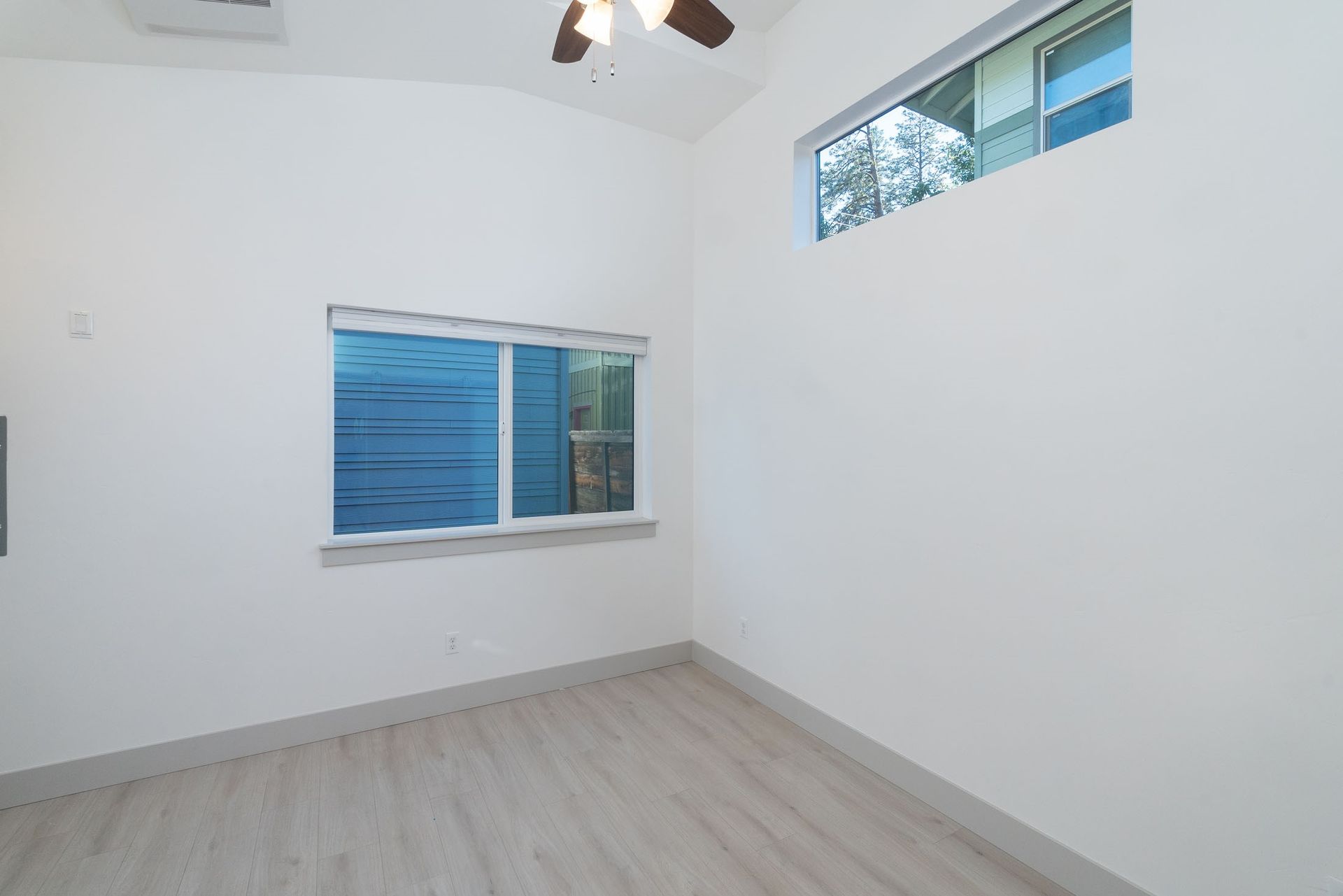 An empty bedroom with two windows and a ceiling fan.