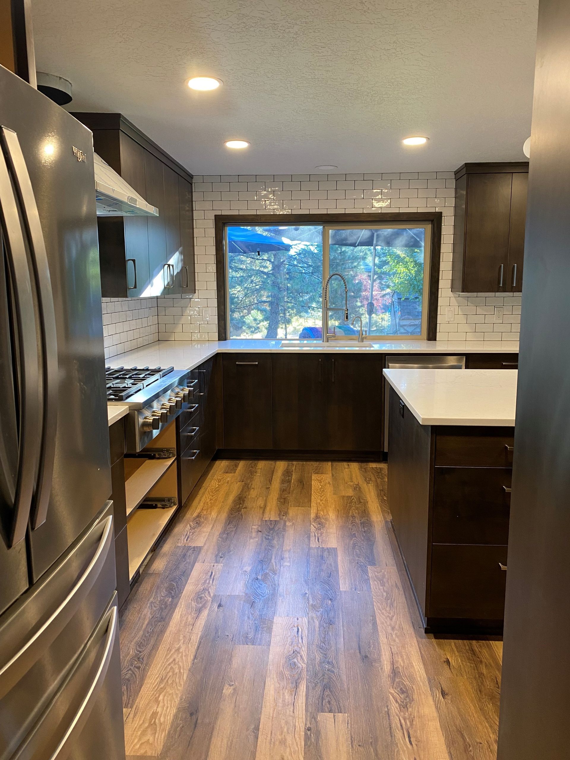 A kitchen with stainless steel appliances , wooden floors , and a large window.