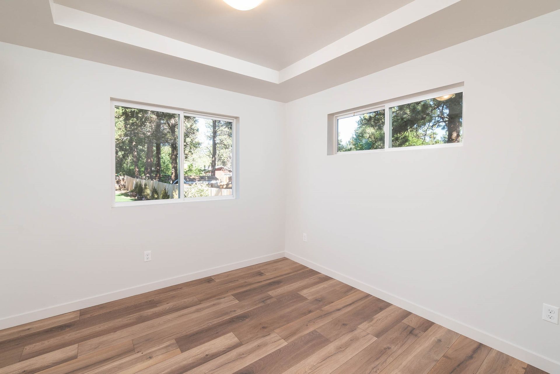 An empty bedroom with hardwood floors and two windows.