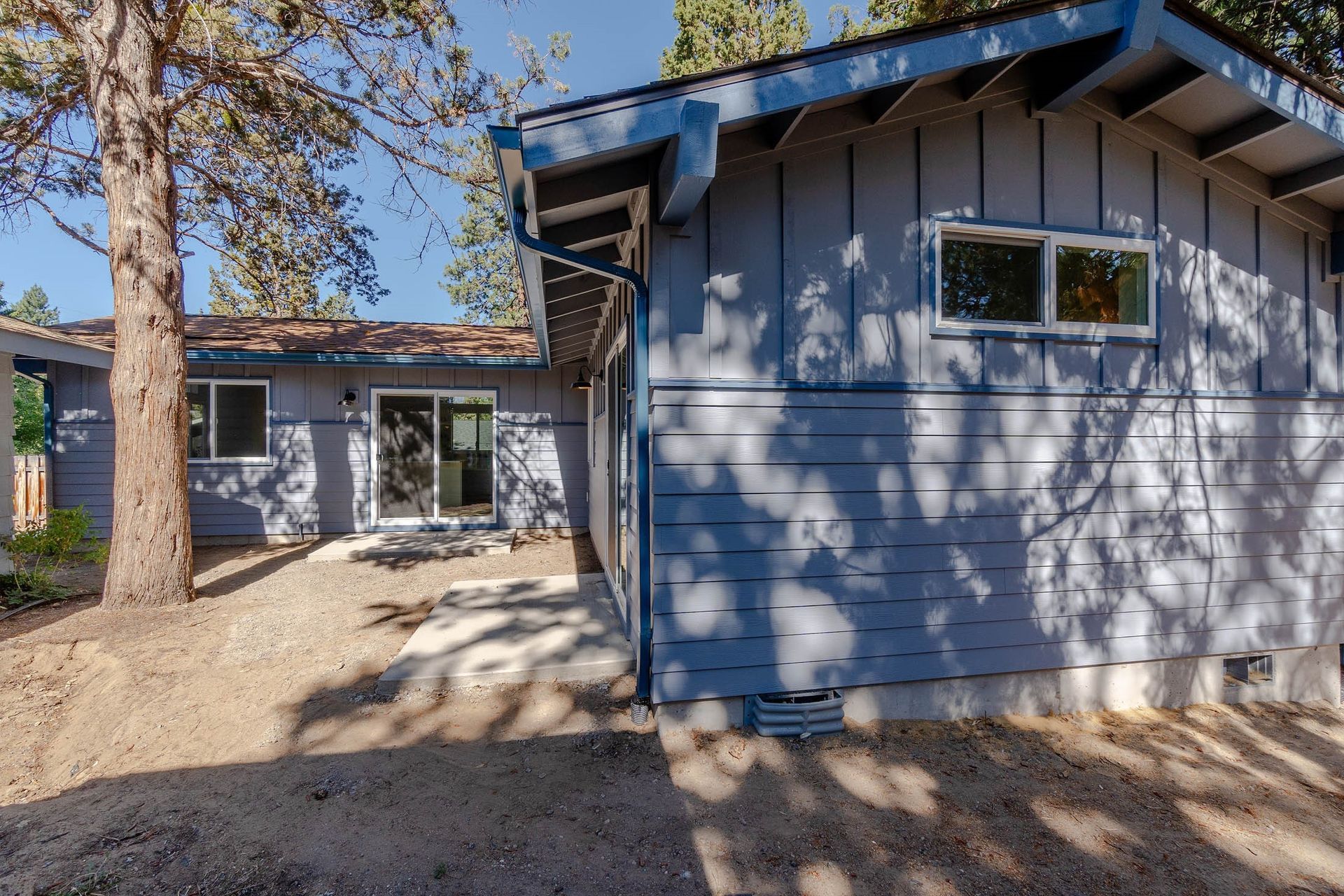 A blue house with a sliding glass door is surrounded by trees.