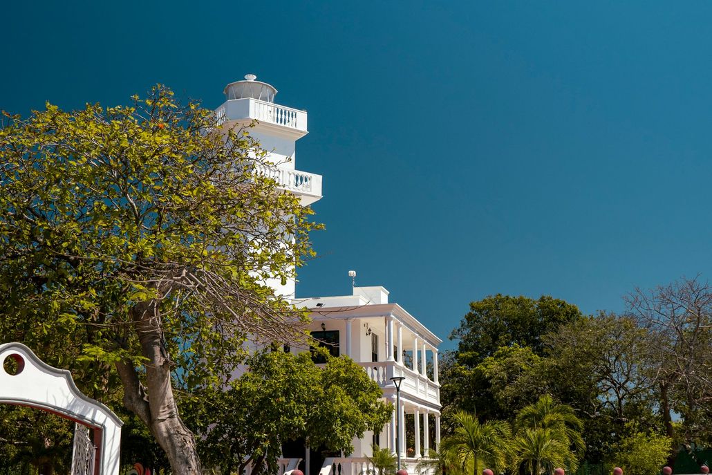 Un gran edificio blanco con un faro en la parte superior está rodeado de árboles.