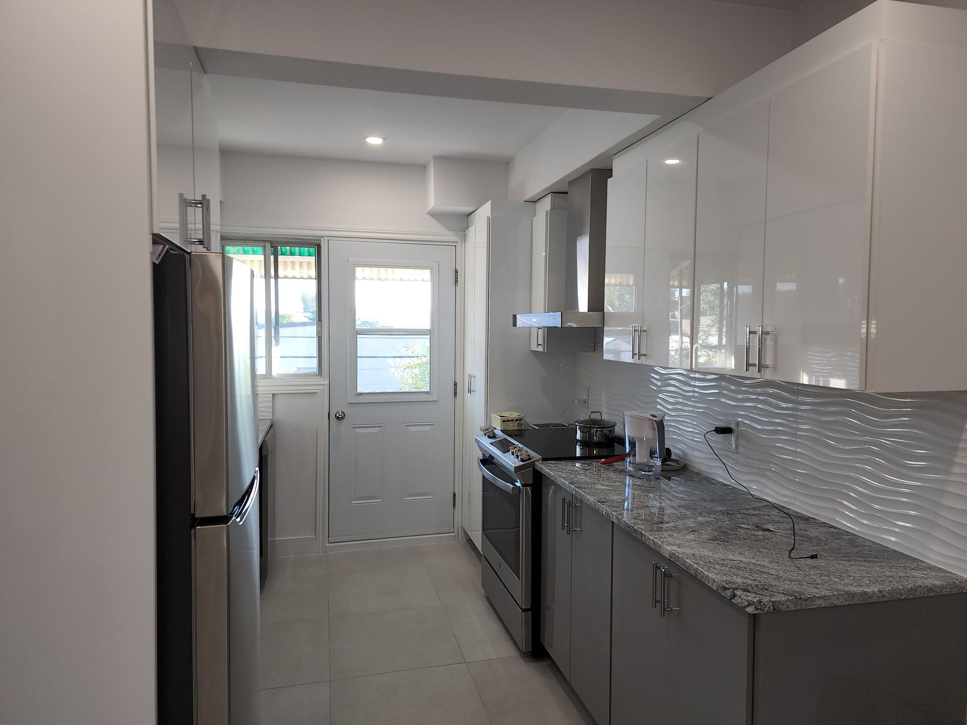 Une cuisine avec armoires blanches, comptoirs en granit, appareils électroménagers en acier inoxydable et réfrigérateur.