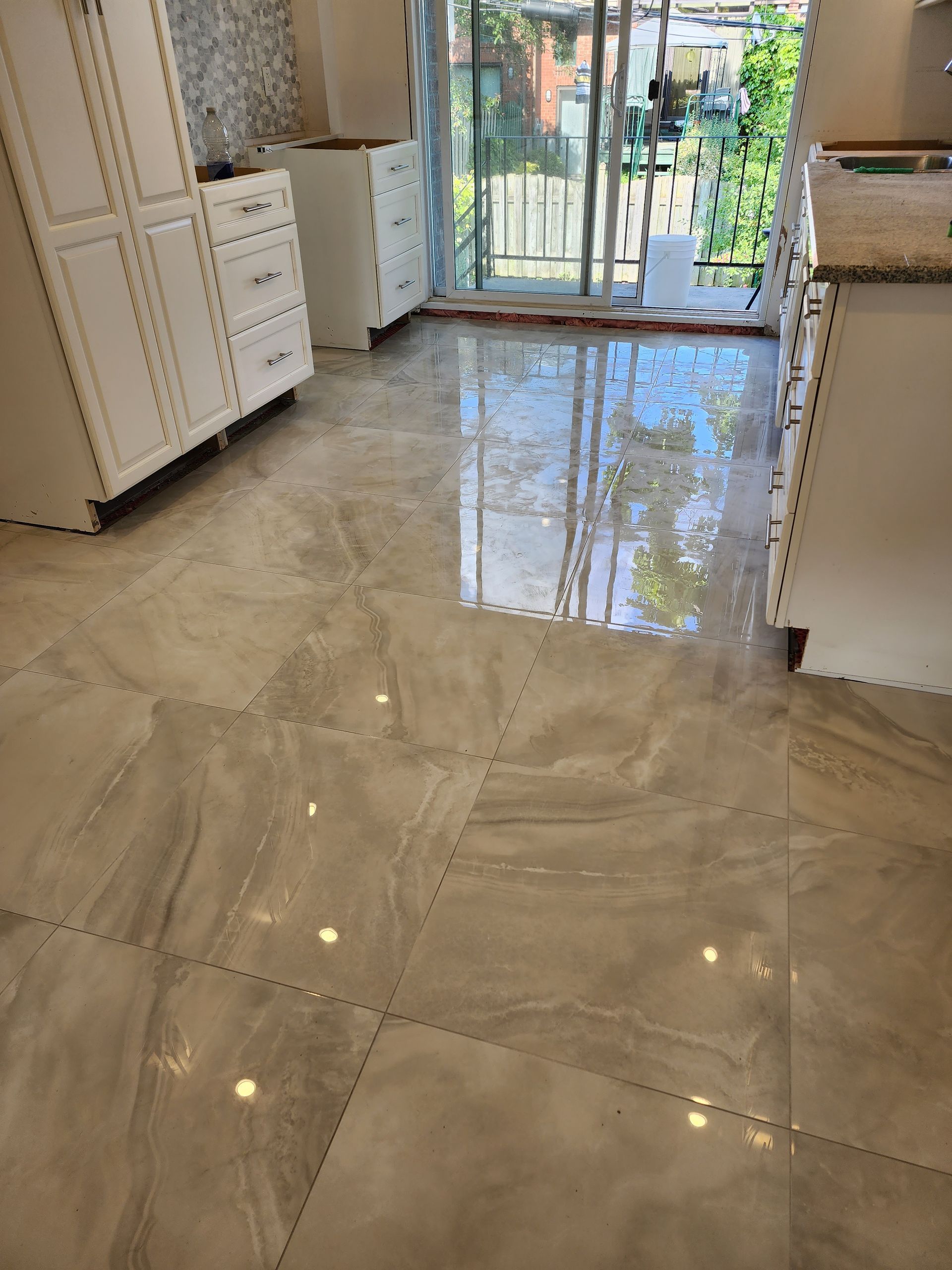 Une cuisine avec un sol carrelé , des armoires blanches et une porte coulissante en verre.