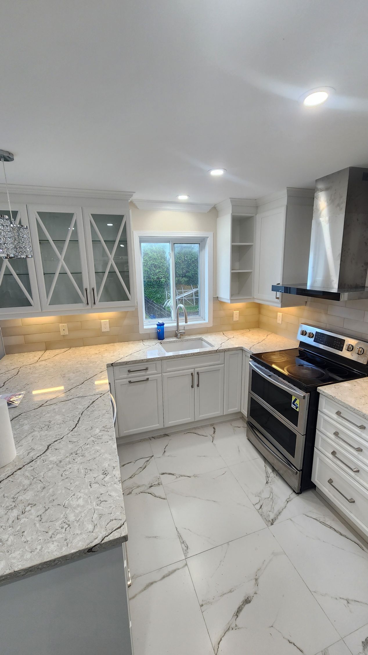 Une cuisine avec armoires blanches, comptoirs en granite, une cuisinière et un évier.