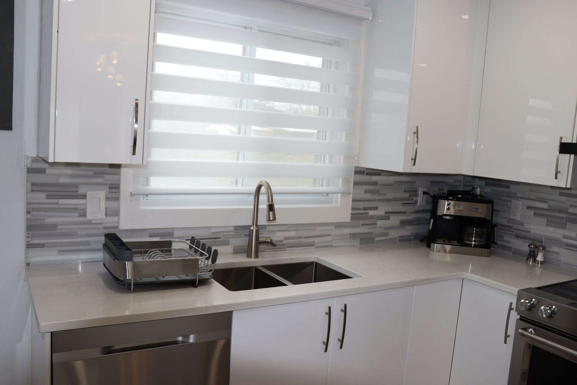 Une cuisine avec armoires blanches, électroménagers en acier inoxydable, un évier et une fenêtre.