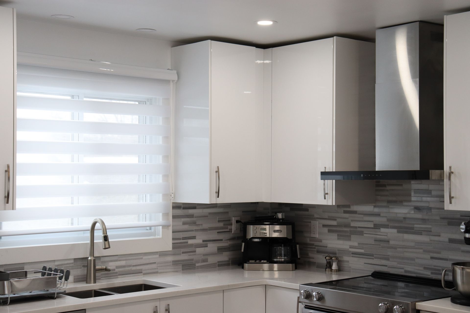 Une cuisine avec des armoires blanches, une cuisinière, un évier et une fenêtre.