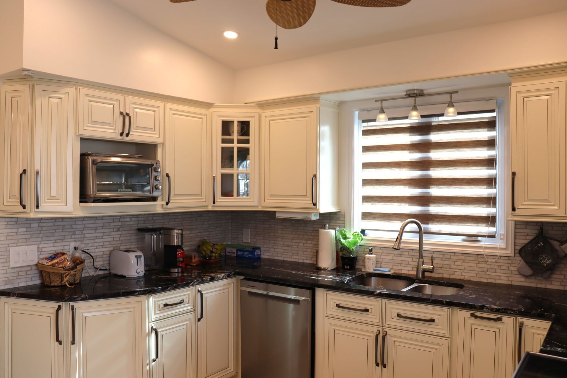 Une cuisine avec des armoires blanches, des comptoirs noirs, des appareils électroménagers en acier inoxydable et un ventilateur de plafond.