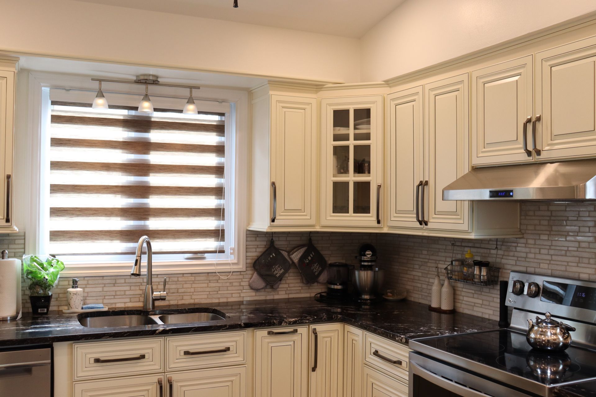 Une cuisine avec des armoires blanches, des comptoirs noirs, des appareils électroménagers en acier inoxydable et une fenêtre.