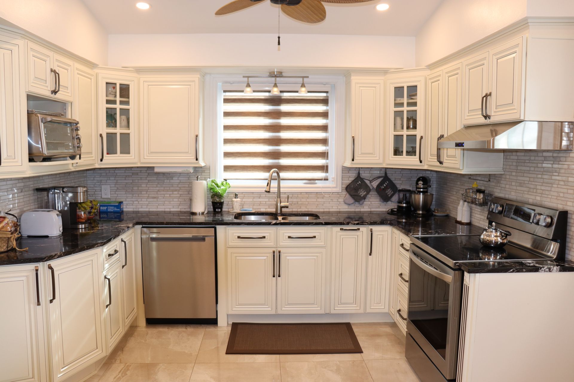 Une cuisine avec des armoires blanches, des comptoirs noirs, des appareils électroménagers en acier inoxydable et un ventilateur de plafond.