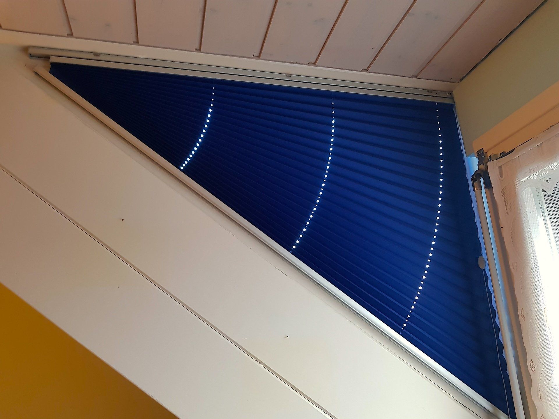 Une fenêtre en forme de triangle avec des stores bleus dessus