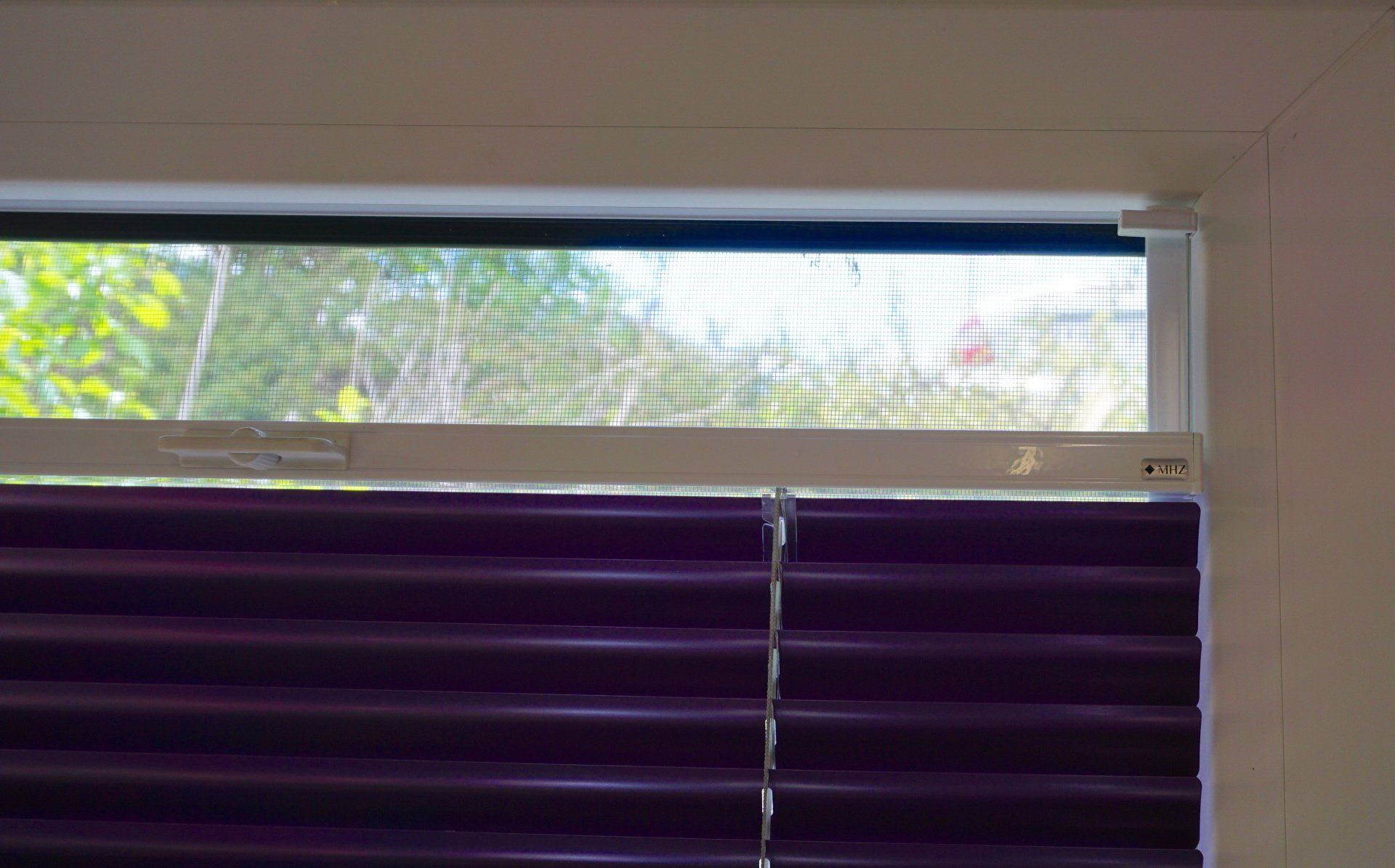 Un gros plan d'une fenêtre avec des stores violets et un écran.