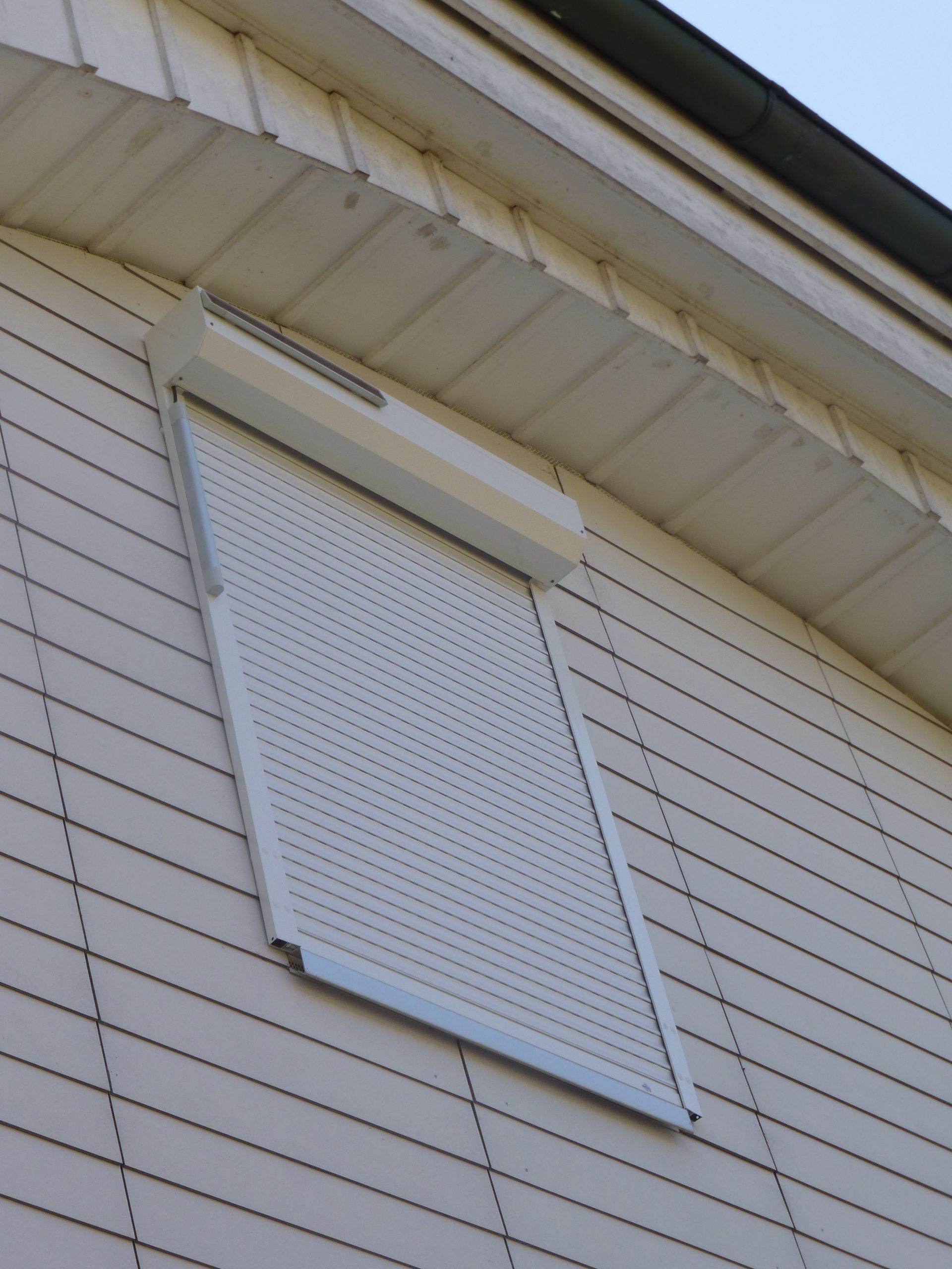 Une maison blanche avec une fenêtre avec un volet roulant dessus