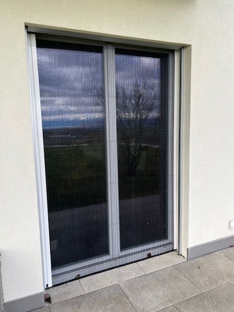 Un bâtiment blanc avec une porte coulissante en verre avec un écran en maille.