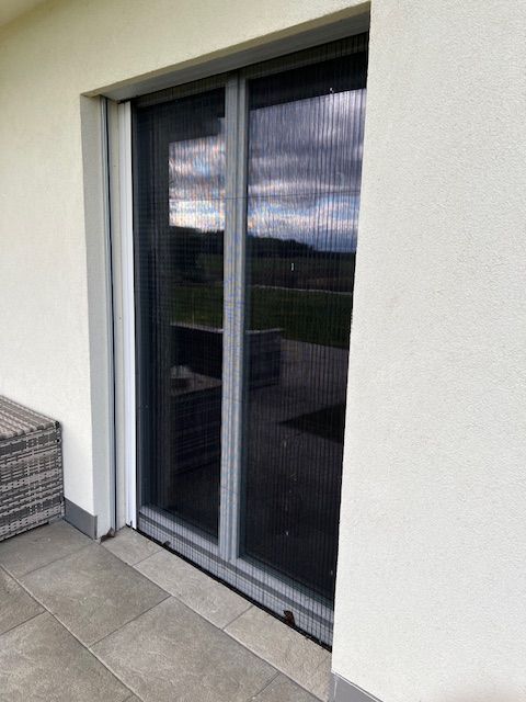 Un bâtiment blanc avec une porte coulissante en verre et un banc en osier.