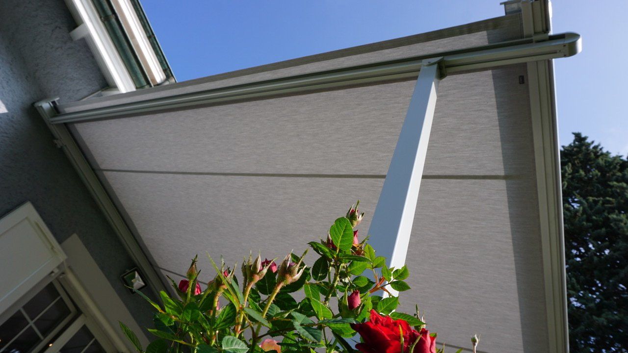 Une rose rouge est assise sous un auvent blanc sur le côté d'une maison.