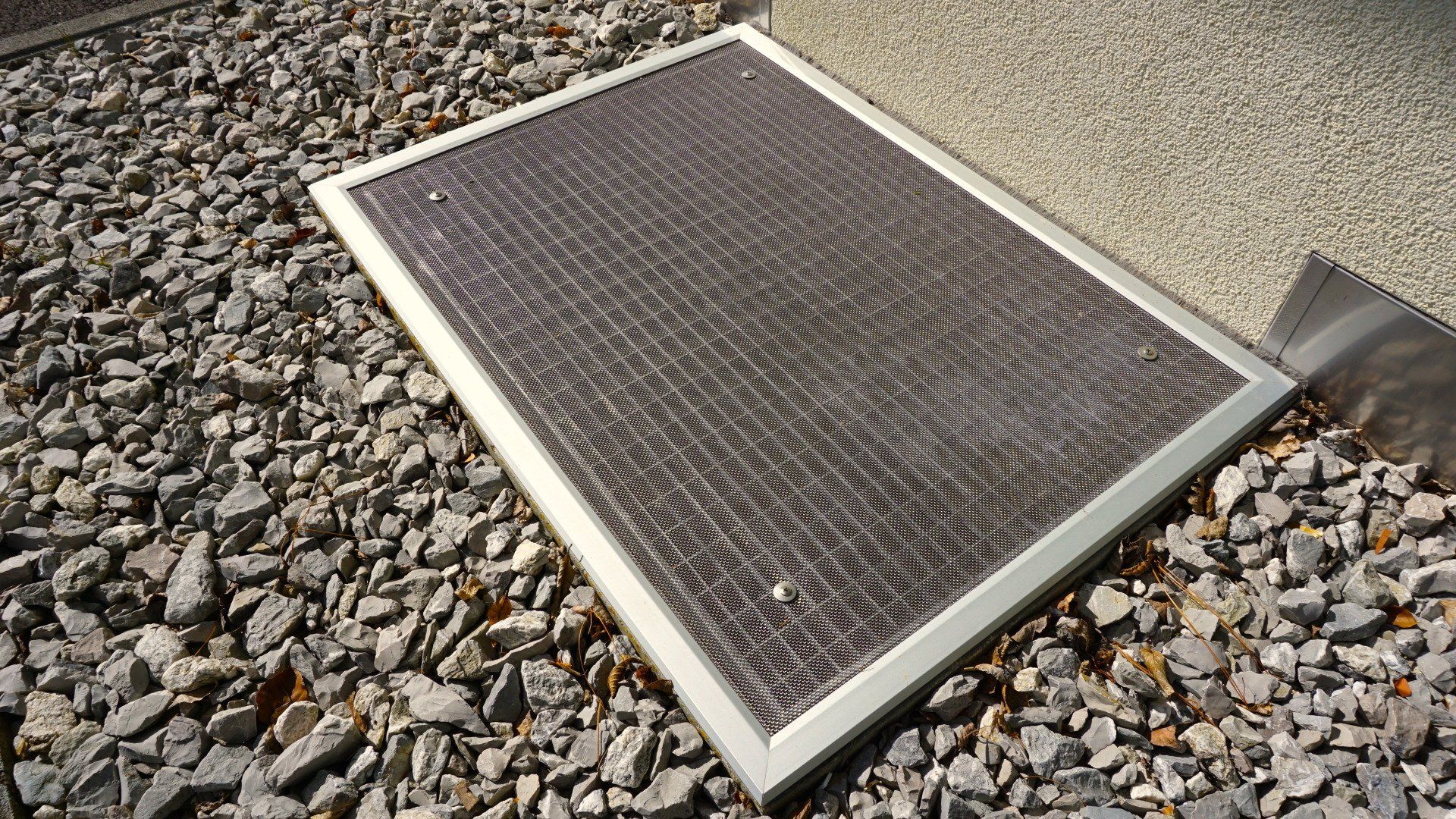 Une porte moustiquaire est posée sur un tas de gravier.