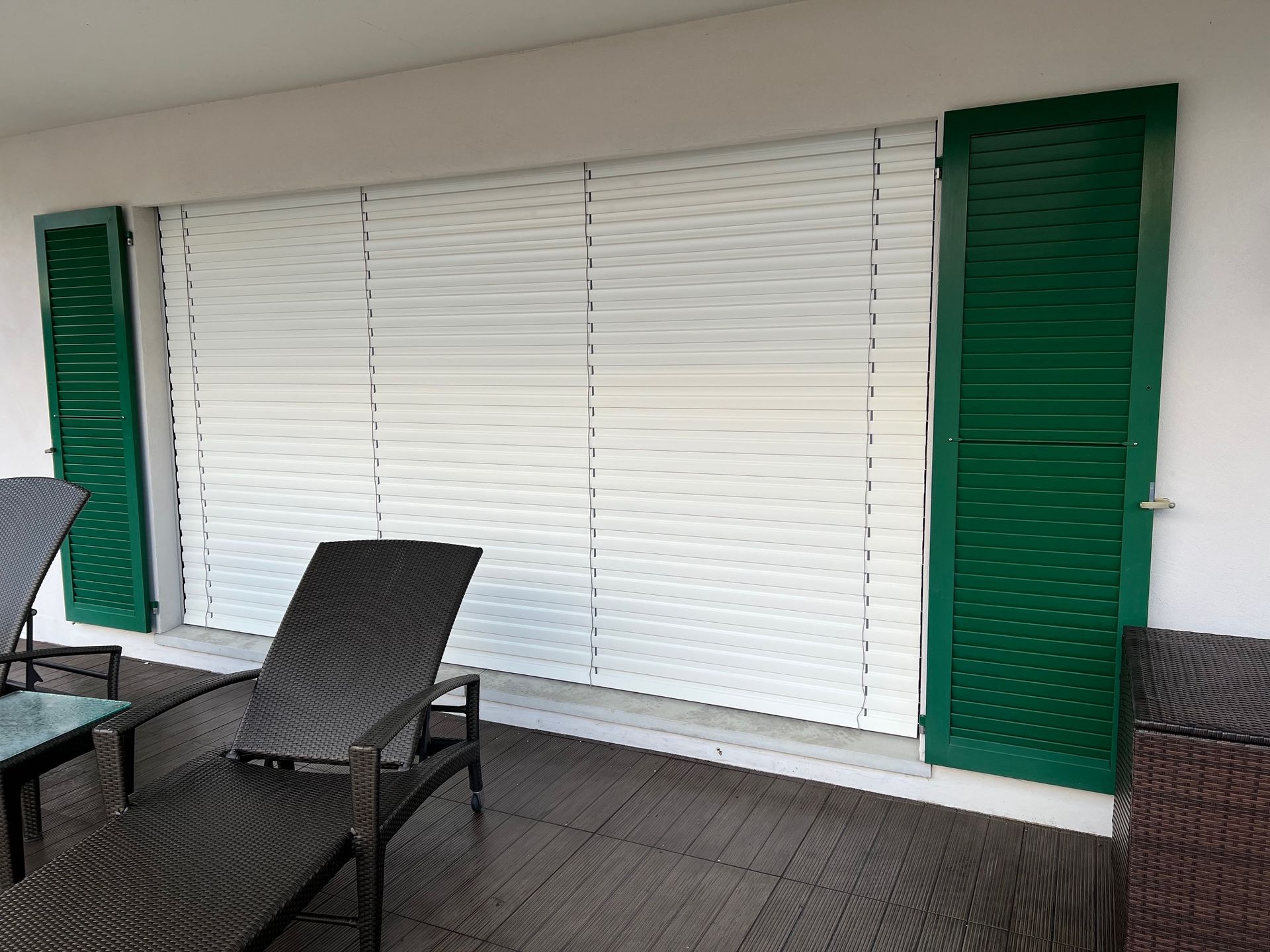 Un balcon avec des volets verts et des stores blancs