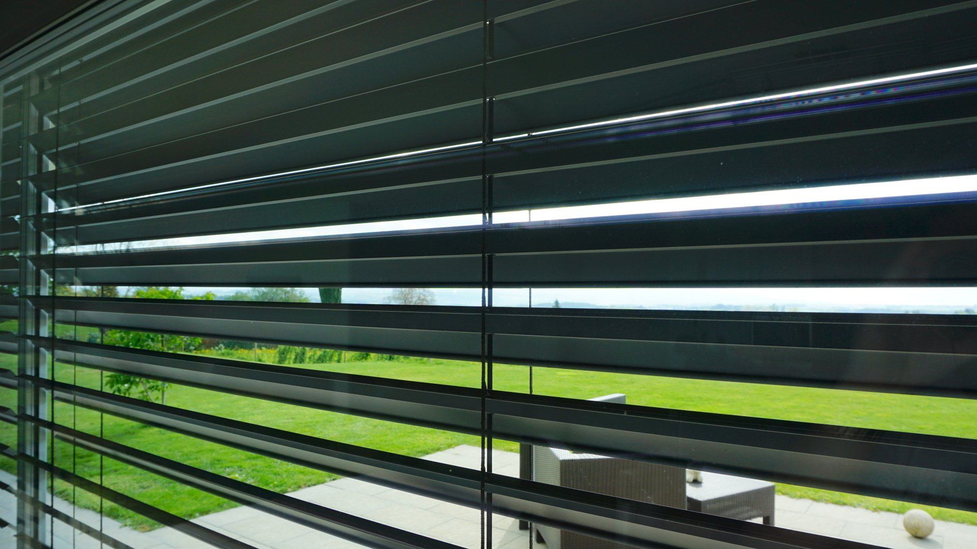 Une fenêtre avec des stores et une vue sur un jardin.
