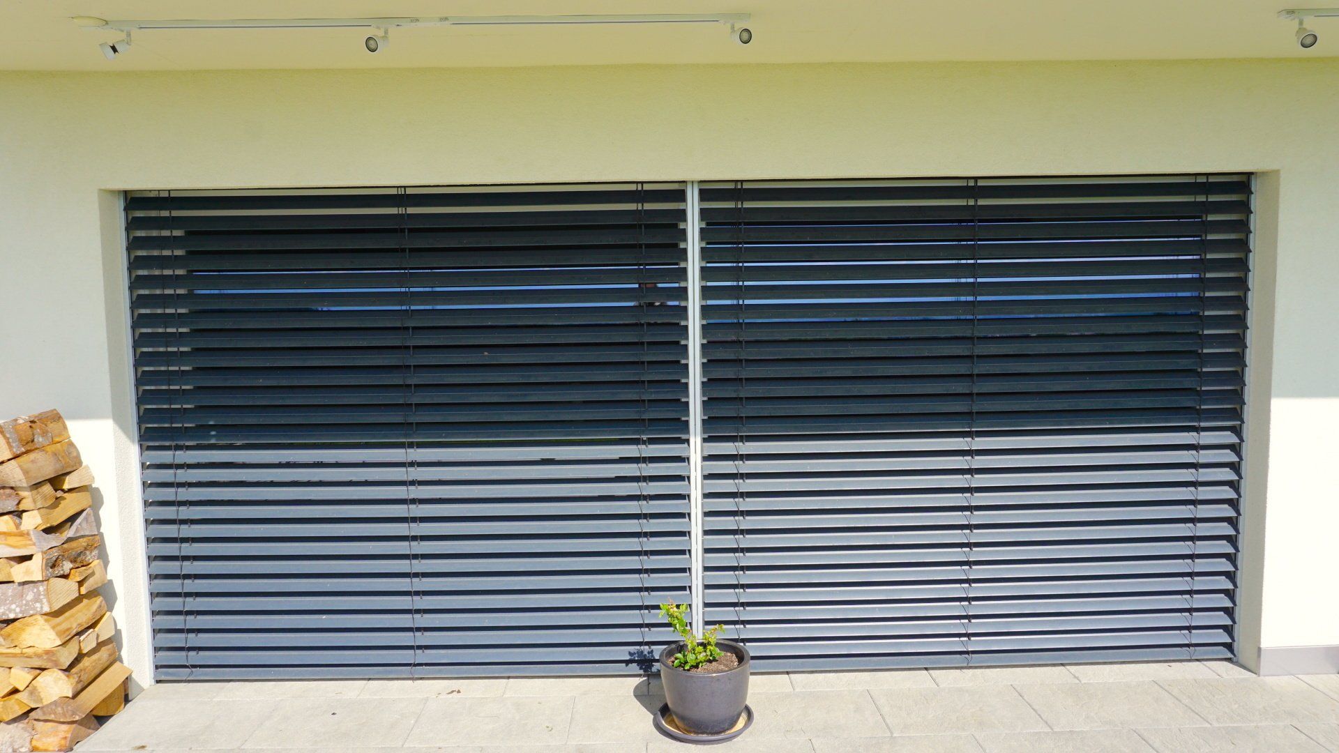 Une plante en pot est posée devant une porte de garage avec des stores.