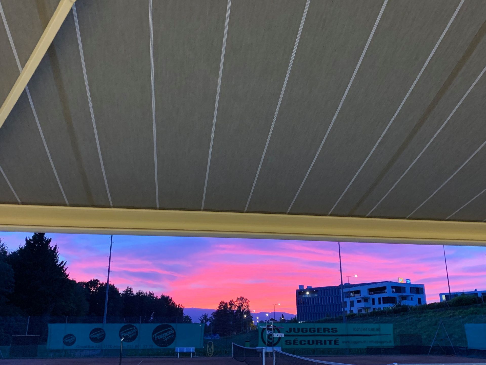Une vue d'un coucher de soleil sur un court de tennis depuis sous un auvent