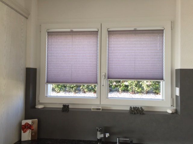 Une cuisine avec deux fenêtres avec des stores violets dessus.