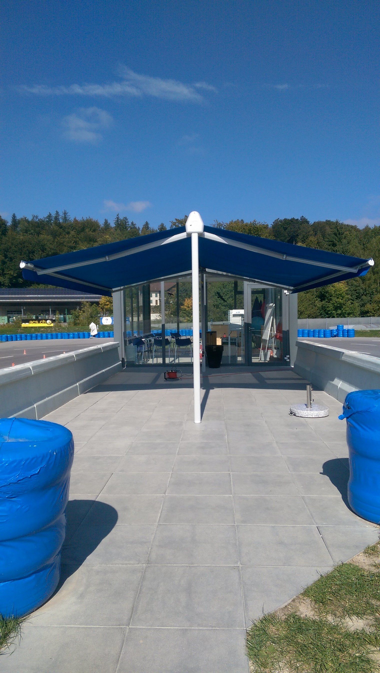 Un parapluie bleu est posé sur un patio en béton à côté de deux réservoirs d'eau bleus.