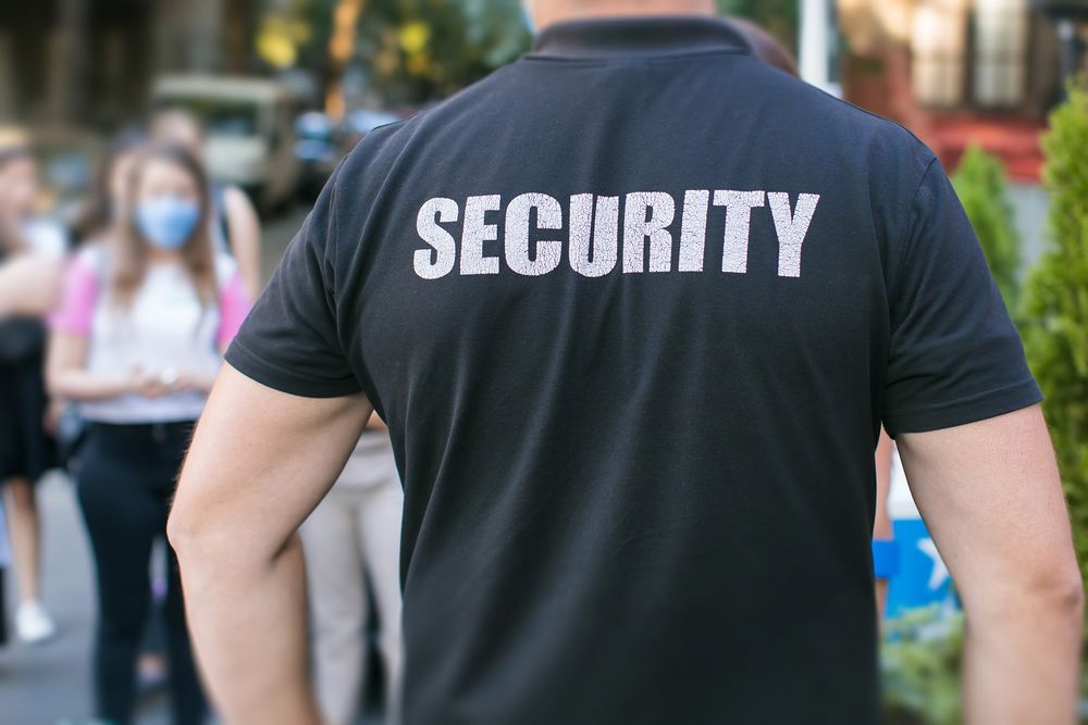 Security Guard Standing on Street in Front of Crowd Wearing Face Masks - Security Company in Gilgandra, NSW