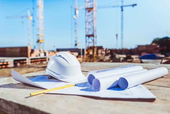 Un casco, un lápiz y planos están sobre una mesa en un sitio de construcción.