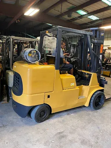 Yellow Caterpillar forklift with driver in a warehouse.