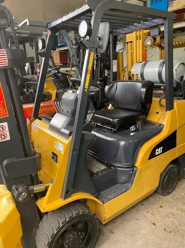 Yellow Caterpillar forklift with a black seat and propane tank, parked indoors.