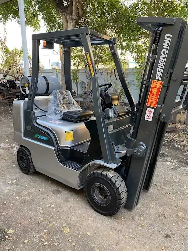 Man operating a forklift, carrying a pallet with a large cardboard box inside a warehouse.