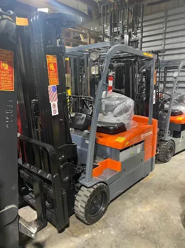 Forklift in warehouse; gray and orange, with raised forks.