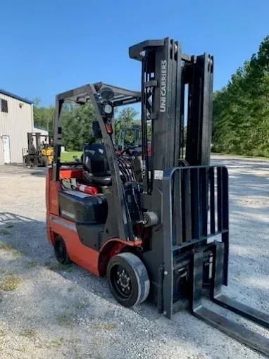 Red and black Unicarriers forklift on gravel, parked outdoors, under a clear sky.