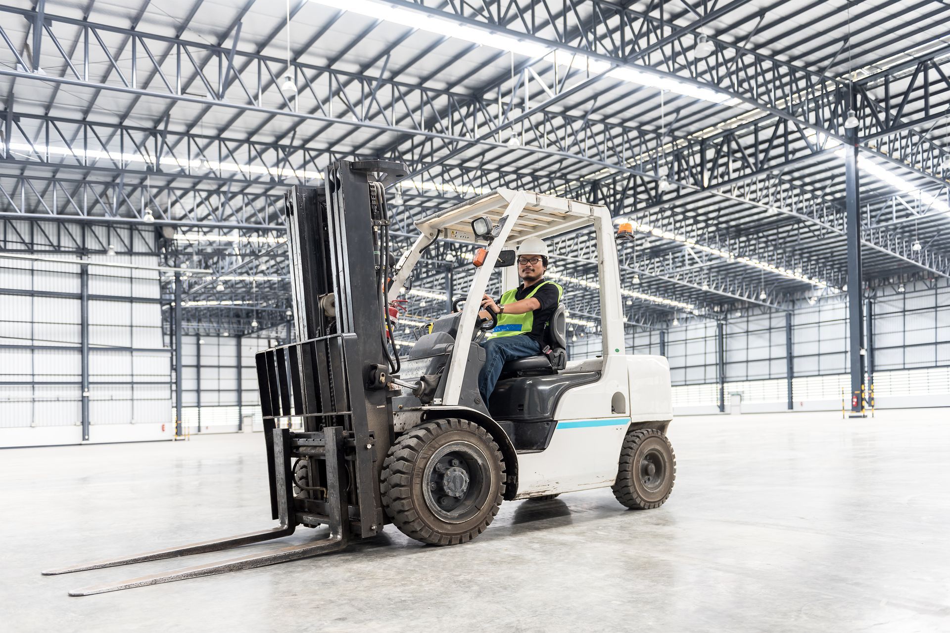 Forklift operator in a warehouse, wearing safety gear.