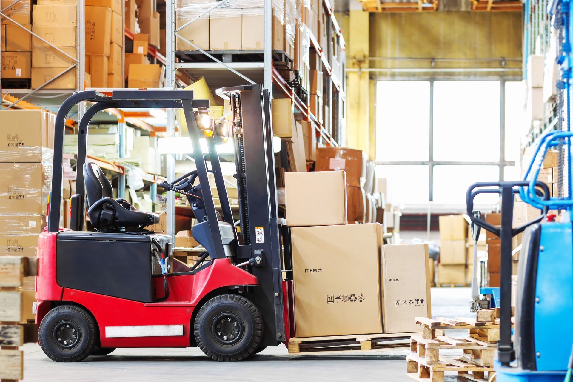 Red forklift carrying cardboard boxes in a warehouse. Red forklift carrying cardboard boxes in a warehouse.