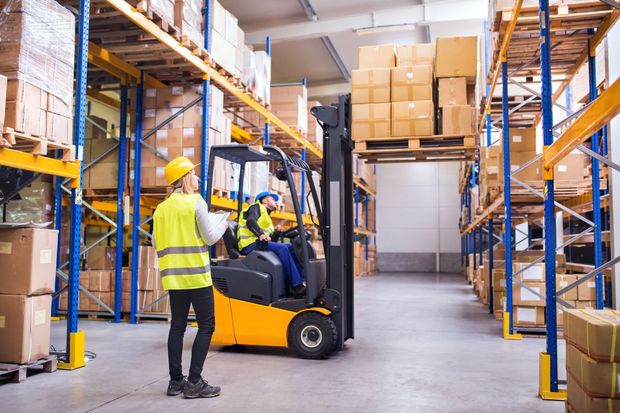 Warehouse with forklift, workers loading shelves with cardboard boxes; yellow safety vests. Warehouse with forklift, workers loading shelves with cardboard boxes; yellow safety vests.