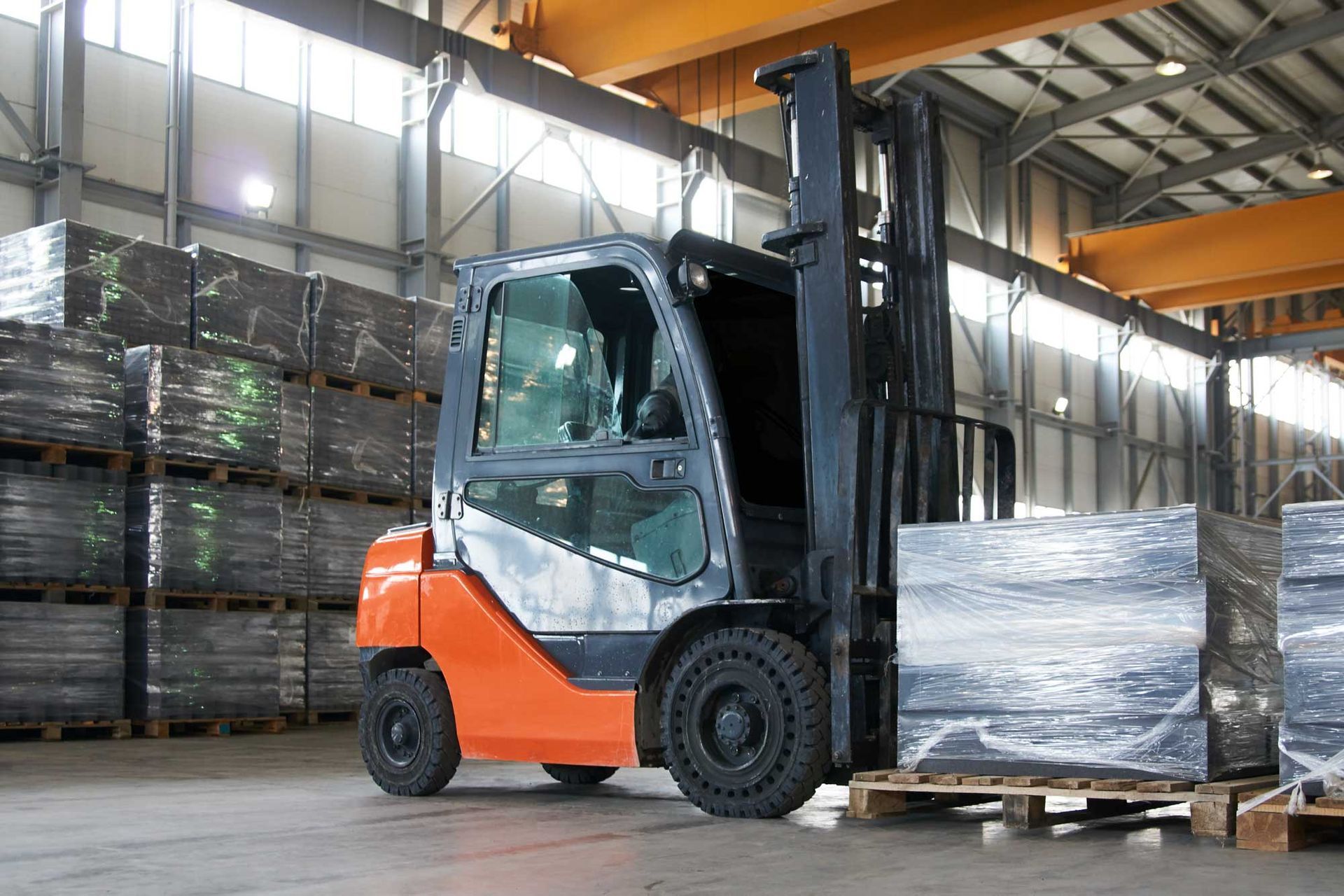 Orange and black forklift in a warehouse, moving palletized wrapped materials. Orange and black forklift in a warehouse, moving palletized wrapped materials.