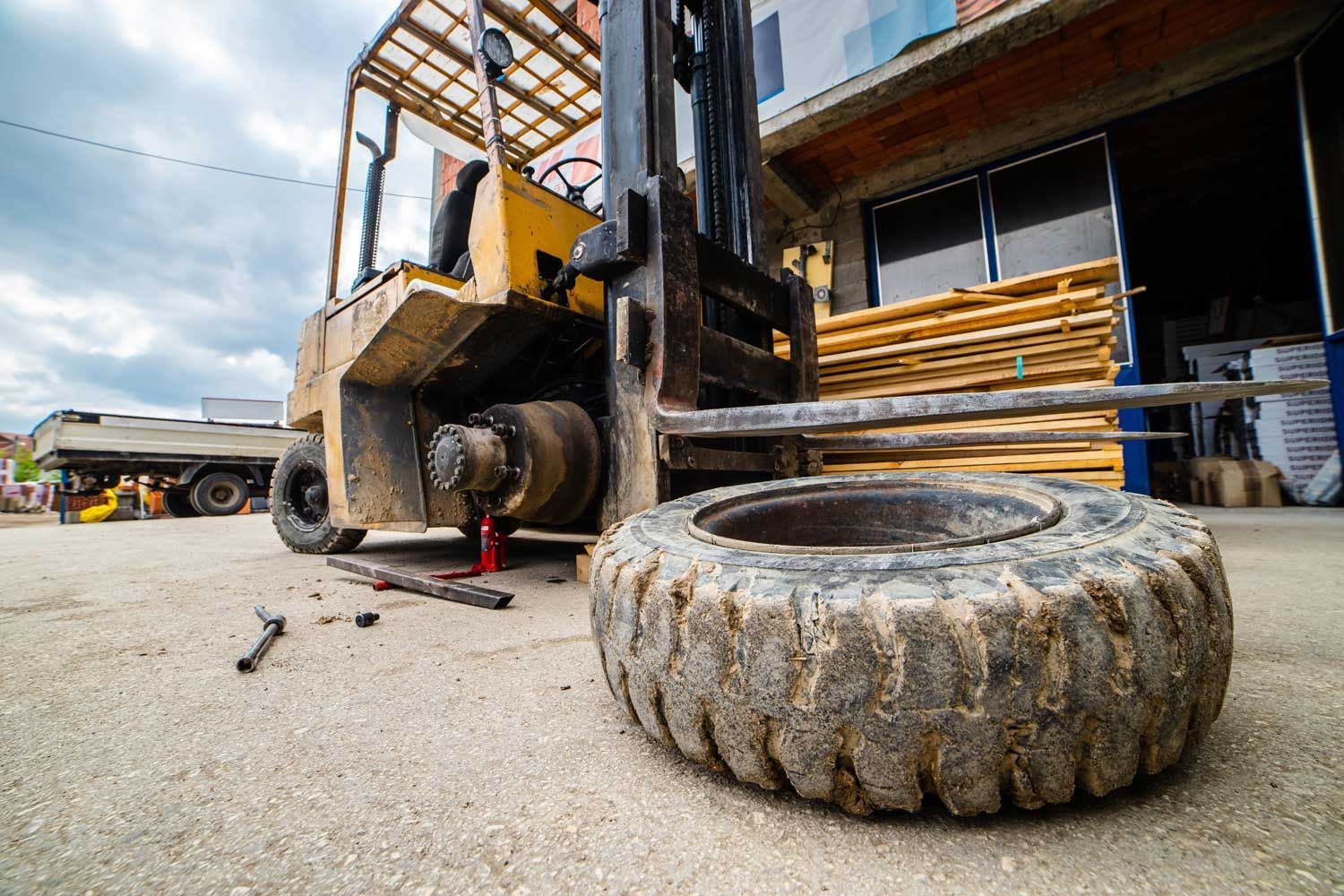 Yellow forklift with a flat tire, tire removed. Tools and lumber in background. Yellow forklift with a flat tire, tire removed. Tools and lumber in background.