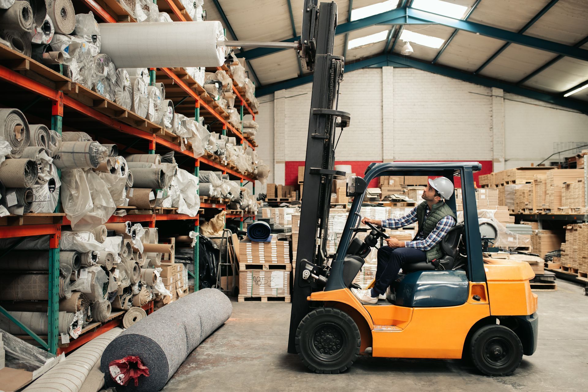 Forklift operator in a warehouse, lifting a large roll of material from a high shelf. Forklift operator in a warehouse, lifting a large roll of material from a high shelf.