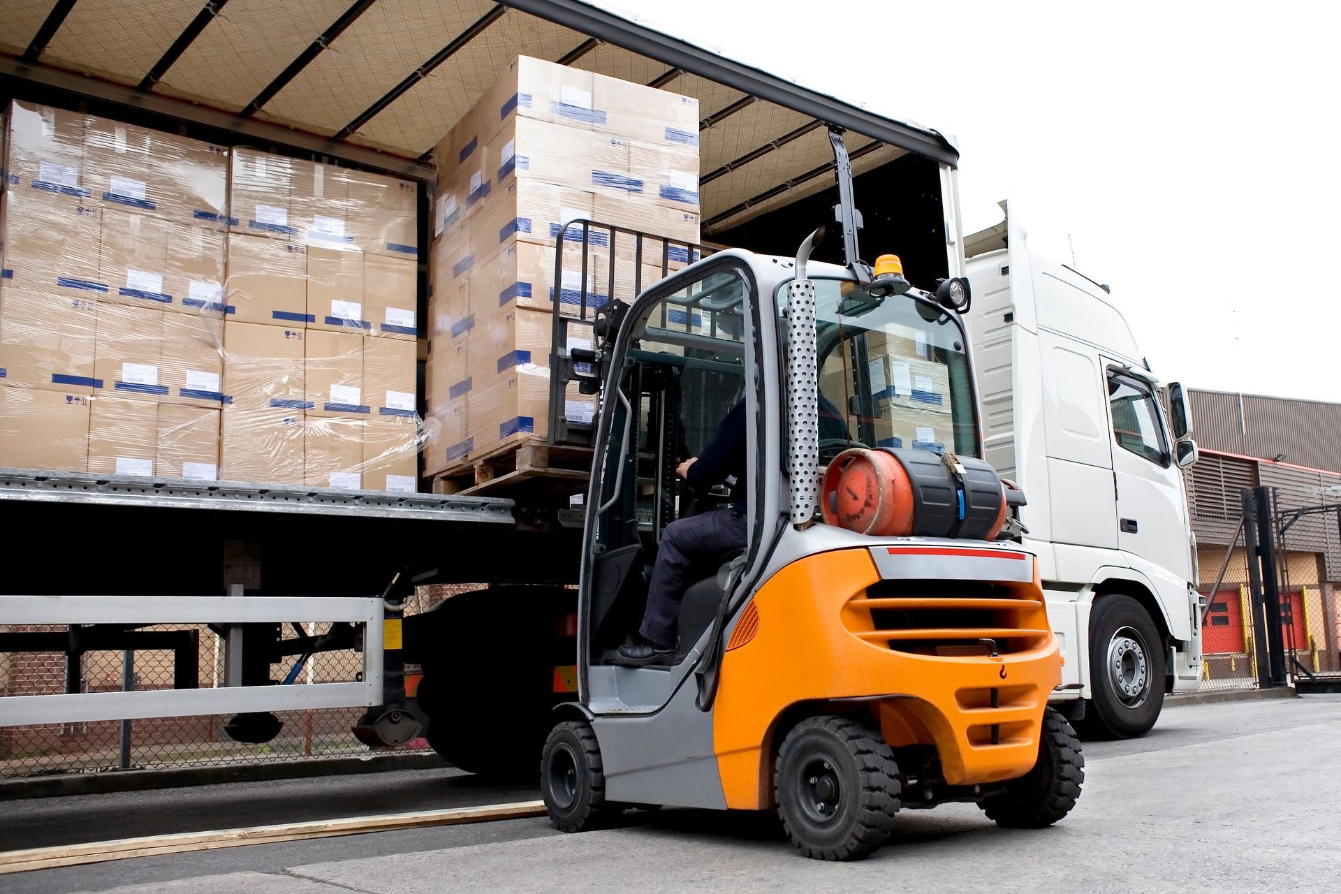 Forklift lifts stacked pallets from a truck trailer during a warehouse loading operation.