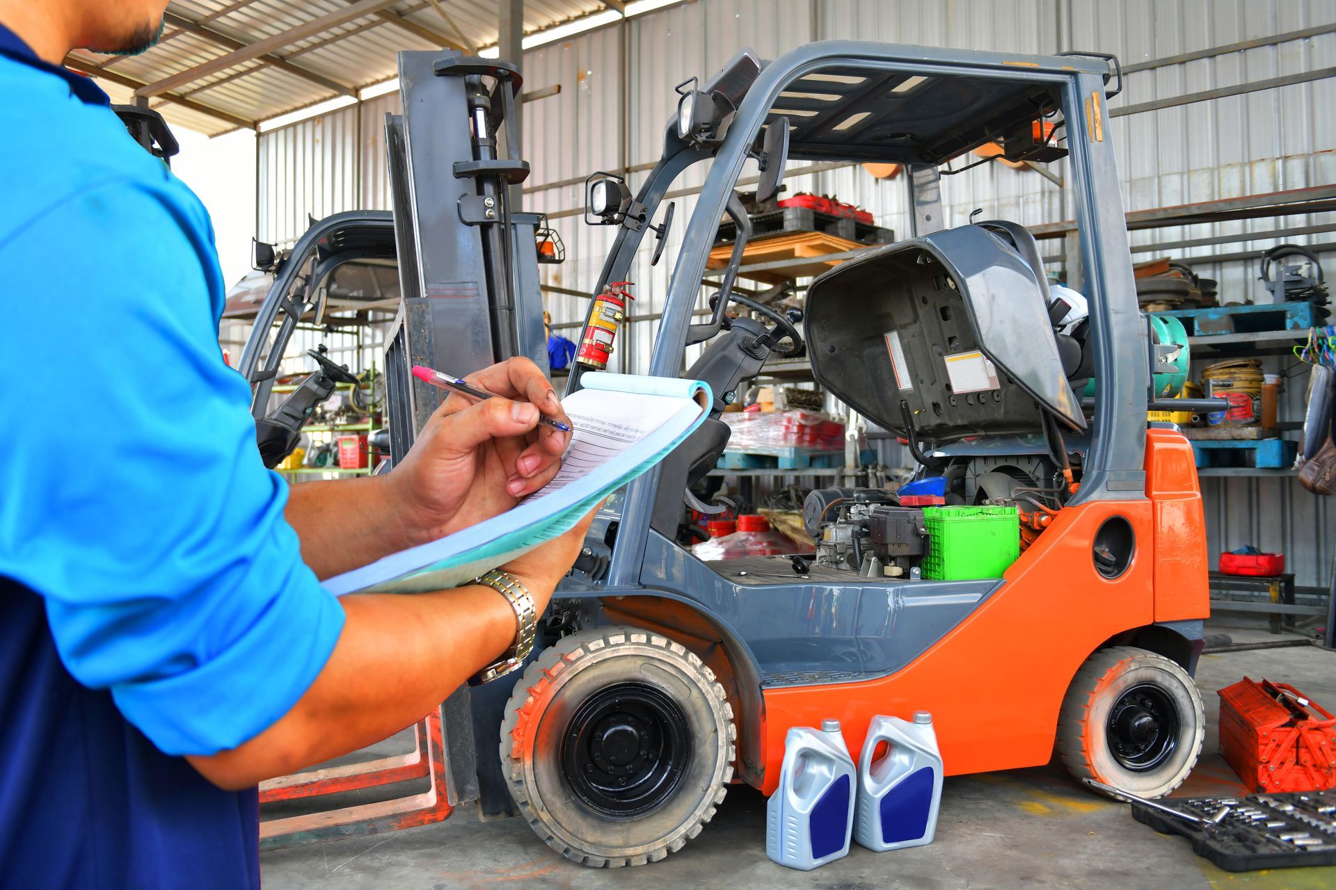 Mechanic inspecting a forklift, writing on a clipboard in a warehouse setting.