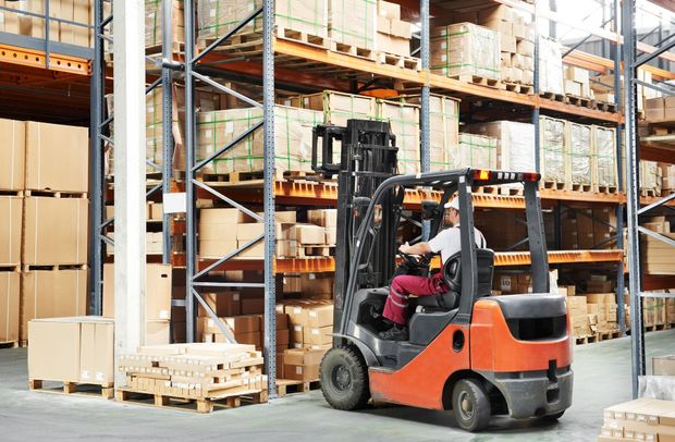 Forklift in a warehouse, moving pallets of boxes on shelves. Orange forklift, worker driving. Forklift in a warehouse, moving pallets of boxes on shelves. Orange forklift, worker driving.