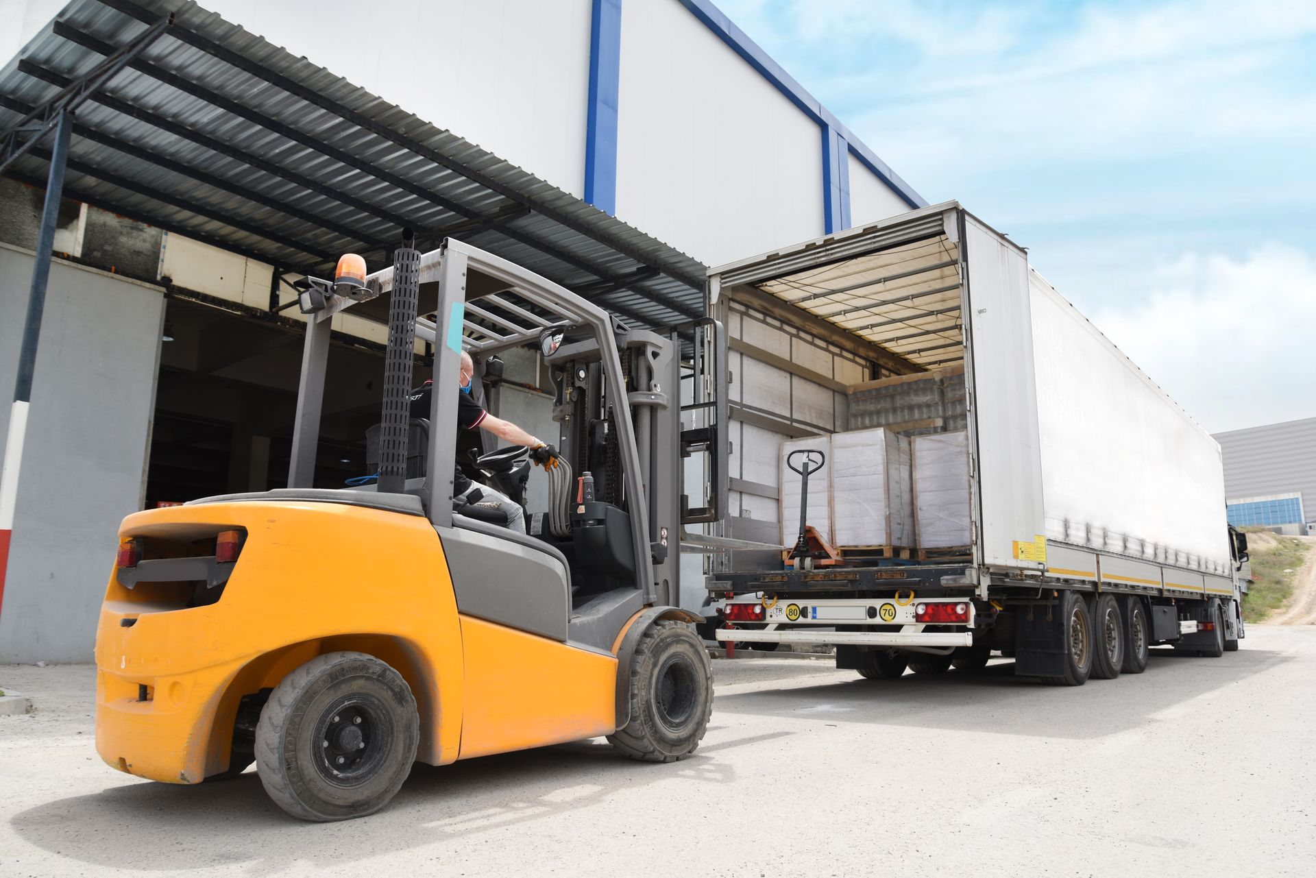 Yellow forklift loading a white trailer at a warehouse.